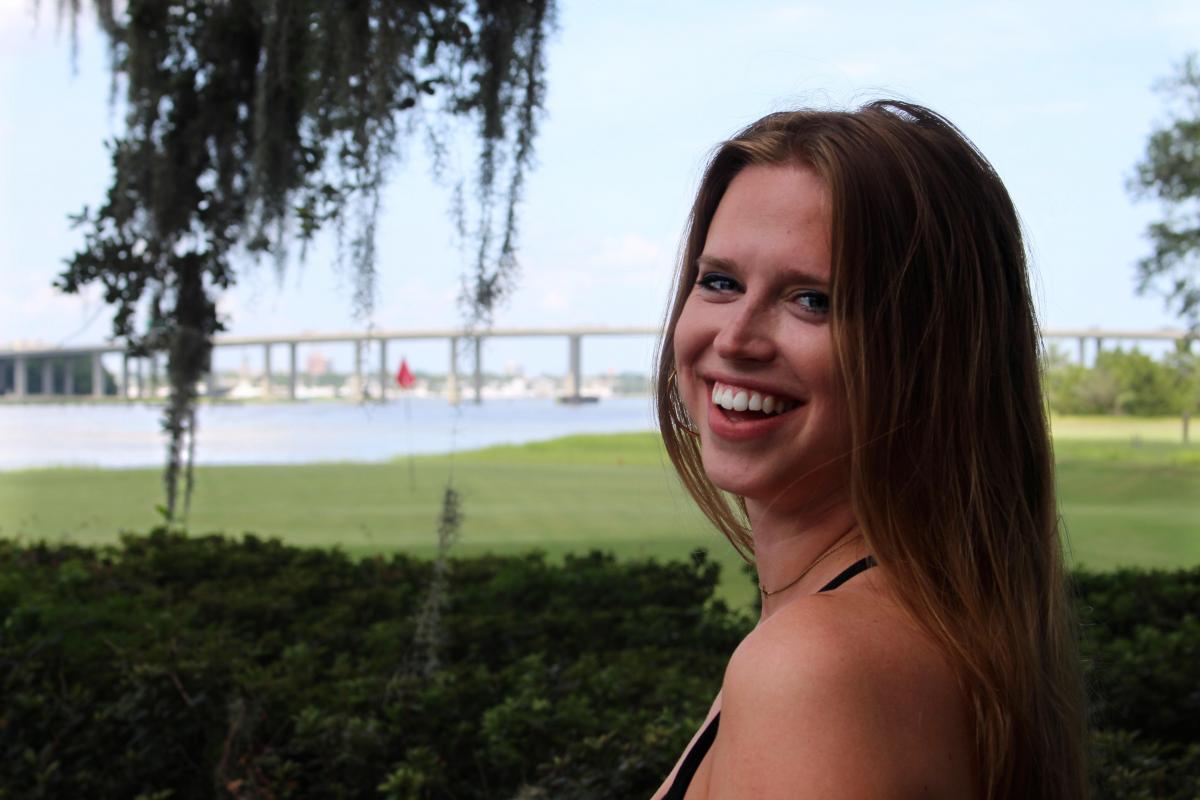 This is a picture of publicist Hannah Larrew taken outside with a tree in the background. The tree has spanish moss hanging from it.