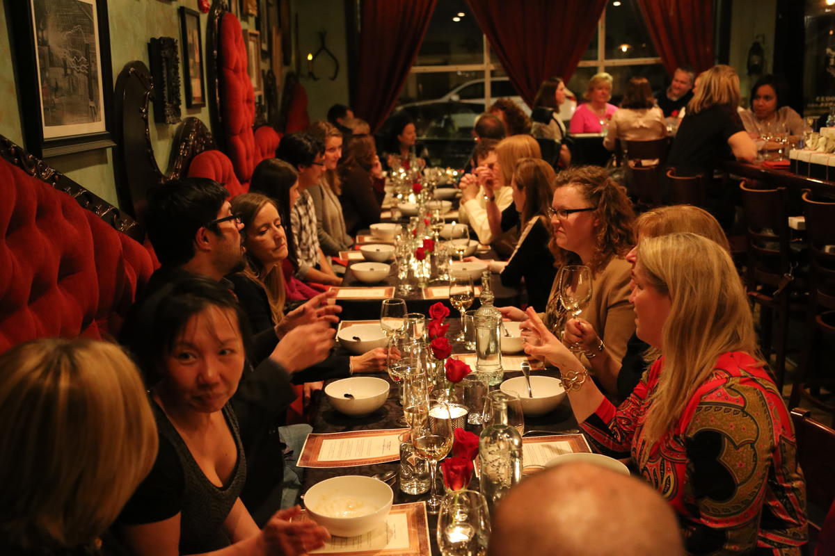 This is a picture of a long dining table in a restaurant with people sitting around it talking and eating.